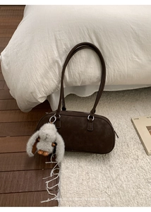 Detail of a dark brown retro Boston bag on a white rug with a cute grey rabbit charm