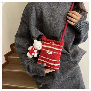 Dettaglio di una borsa a tracolla in maglia a righe con bottone in legno e ciondolo a orsetto
