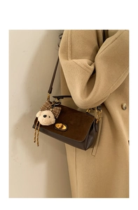 Detail view of brown crossbody bag with matte texture and cute plush bear keychain charm