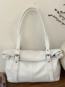 Minimalist white leather tote bag with vintage metal buckles on a wooden table