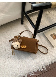 Detail of brown leather bag with suede flap, metal twist lock and cute bear charm