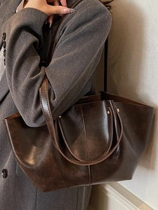 Schicke dunkelbraune Leder-Shopper-Tasche 2025 mit langen Riemen an einem Model in Grau