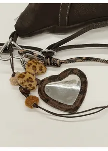 Détail d'un miroir léopard en forme de cœur et d'un nœud en peluche sur un sac brun