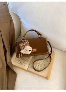 Brown suede crossbody bag with golden buckle and cute puppy charm on a book
