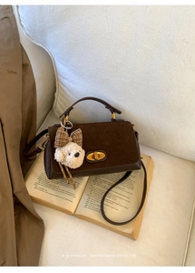 Detail of brown suede tote with gold clasp, teddy bear charm, and adjustable strap