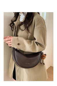 Détail du sac dumpling marron avec logo doré et breloque peluche sur manteau beige
