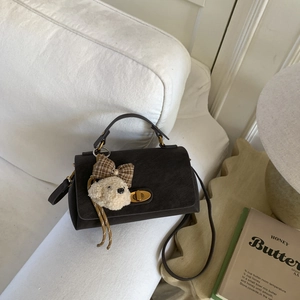 Detail of a dark brown crossbody bag with golden clasp and a plush dog charm on a sofa