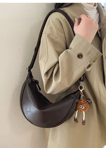 Détail du sac croissant en cuir marron avec logo doré et pendentif peluche fantaisie