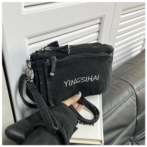 Detail of black denim crossbody bag featuring multi-layer zippers and white embroidery