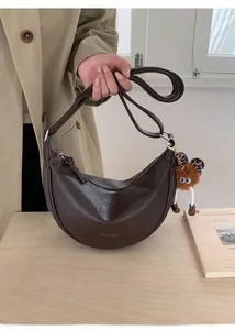 Détail du sac demi-lune marron foncé avec logo de marque et porte-clés monstre en peluche