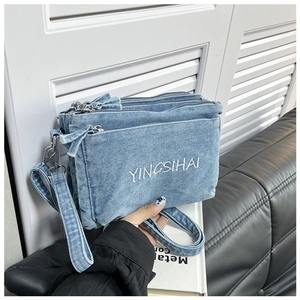 Detail shot of blue denim crossbody bag with three zipper layers and brand lettering