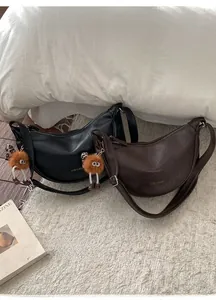 Gros plan de sacs demi-lune noir et marron avec breloques monstres sur fond en peluche