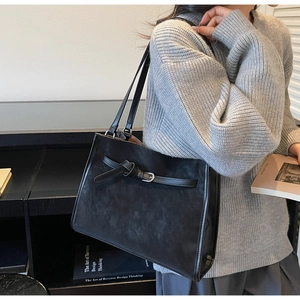 Macro detail of the stylish black tote bag with buckle strap on a model's shoulder