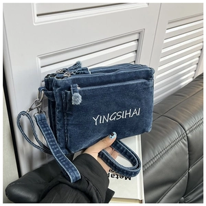Detail of blue denim crossbody bag with three zipper pockets and white embroidery