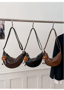Trois sacs hobo demi-lune minimalistes en noir et marron avec des charms en peluche
