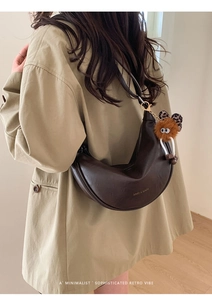 Détail d'un sac bandoulière croissant café vintage avec un charmant pendentif monstre en peluche