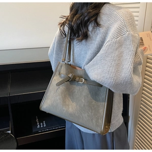 Detail of grey-green tote bag showing silver buckle and long shoulder strap on model