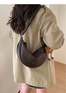 Détail du sac bandoulière demi-lune en cuir marron foncé avec un charmant monstre en peluche