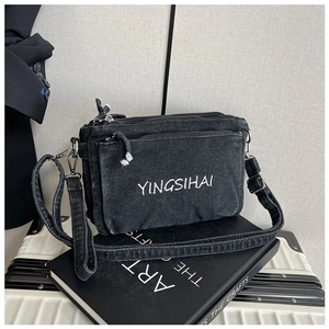 Detail of black denim crossbody bag with white embroidery and multi-layer zippers
