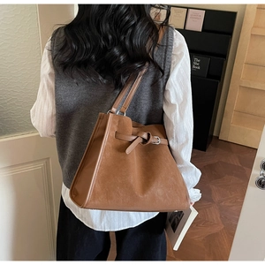 Detailed view of brown suede tote bag with decorative buckle and slim shoulder straps