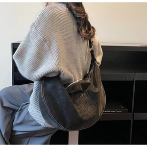 Dettaglio della borsa hobo nera con cuciture a contrasto e ricamo floreale su pelle opaca