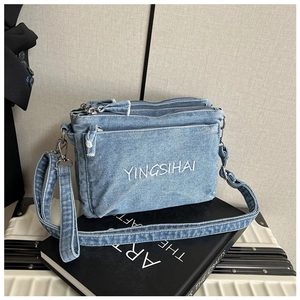 Detail of light blue denim crossbody bag with multi-pocket design and white embroidery