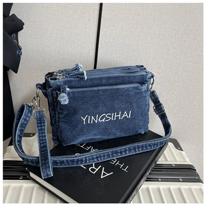 Detail of blue denim crossbody bag featuring triple-zipper storage and white embroidery
