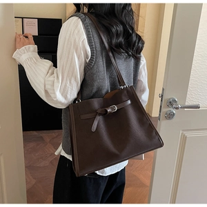 Deep brown oversized tote bag with decorative buckle strap detail on a casual model