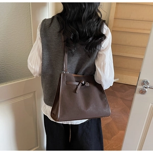Detail view of deep brown suede tote bag with decorative buckle strap and long handle