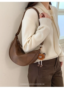 Détail du sac bandoulière croissant en cuir marron avec texte doré et grigri monstre