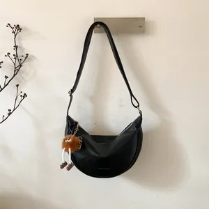 Détail du sac bandoulière noir en demi-lune avec un pendentif en peluche marron mignon