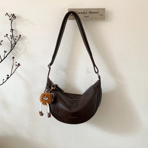 Détail d'un sac demi-lune en cuir marron avec un charme monstre en peluche et logo doré