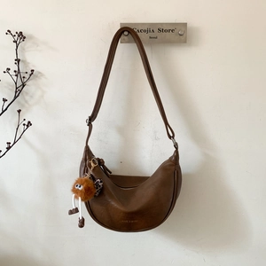 Détail macro d'un sac demi-lune en cuir marron avec un charm de monstre en peluche mignon