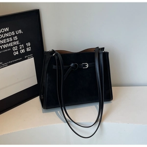 Close-up of black matte leather tote bag featuring decorative silver buckle and thin straps
