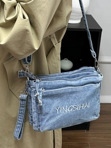 Blue denim crossbody bag with multiple zipper pockets and white embroidery on light coat