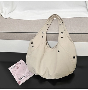 Detail of cream hobo bag with wide strap and silver metal eyelets on a studio table