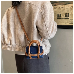 Detail einer Mini-Umhängetasche aus blauem Denim mit braunen Ledergriffen am Modell