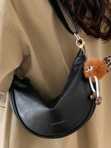Sac bandoulière en cuir noir avec breloque peluche sur mannequin en trench-coat kaki