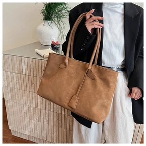 Detail of large brown suede tote bag on a minimalist tiled surface with plant decor