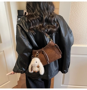 Detail of vintage brown suede crossbody bag with cute plush bunny charm on leather strap