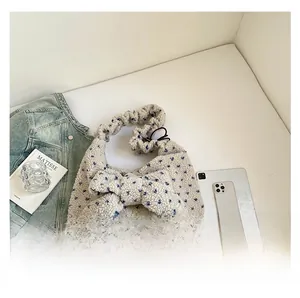Detail of plush floral shoulder bag with a large bow and ruffled strap on a white desk