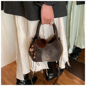 Détail du sac seau en cuir marron foncé avec pompon en peluche et bandoulière dorée