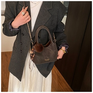 Sac seau en cuir mat marron avec chaîne dorée et pompon porté par un mannequin