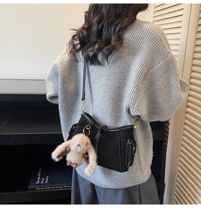 Detail of black crossbody bag with white stitching and plush bunny charm on a model