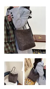 Detail view of a retro brown suede bucket bag worn by a model in autumn scenery