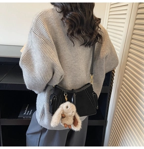 Detail of black suede shoulder bag with white contrast stitching and cute bunny charm