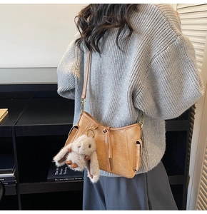 Detail of vintage brown suede crossbody bag with fluffy rabbit pendant and gold metal hooks