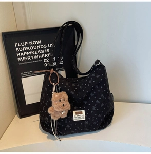 Detail of black bow pattern tote bag with brown plush bear charm and S.NORTH woven label