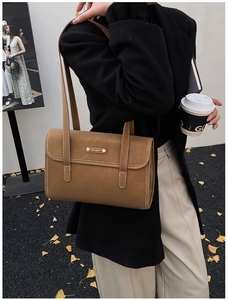 Close-up of caramel brown messenger bag with white contrast stitching and gold metal logo