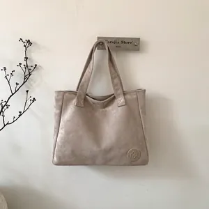 Detail of minimalist beige suede tote bag featuring a round embossed logo and sturdy handles